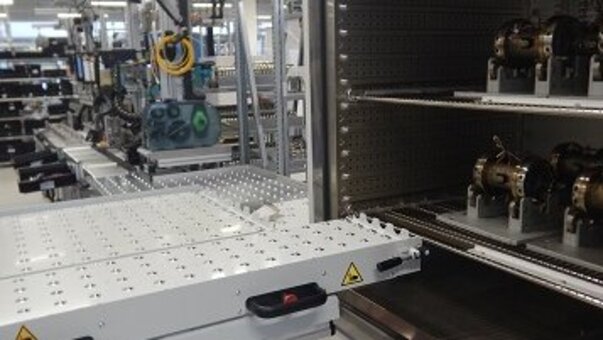 Installation de production industrielle avec, au premier plan, une chambre d'essai ouverte contenant des pièces à usiner. Une plate-forme élévatrice se trouve devant la chambre d'essai.