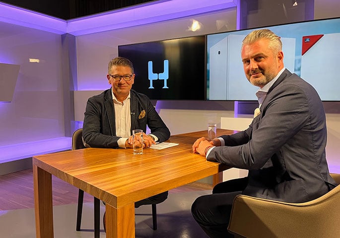 Regio-TV-Moderator Rolf Benzmann und Michael Binder-Pfaff sitzen sich an einem Tisch im Aufnahmestudio gegenüber und blicken in die Kamera.
